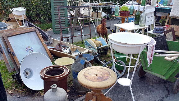 Flohmarkt mit verschiedenen alten Haushaltsgegenständen und Möbeln im Freien.  